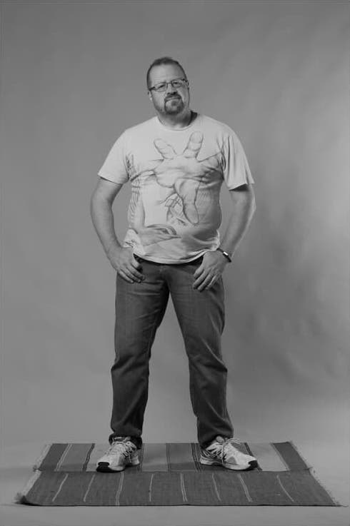 A monochrome photograph of Greg standing on a mat wearing a T-shirt with  a giant hand reaching out on it.