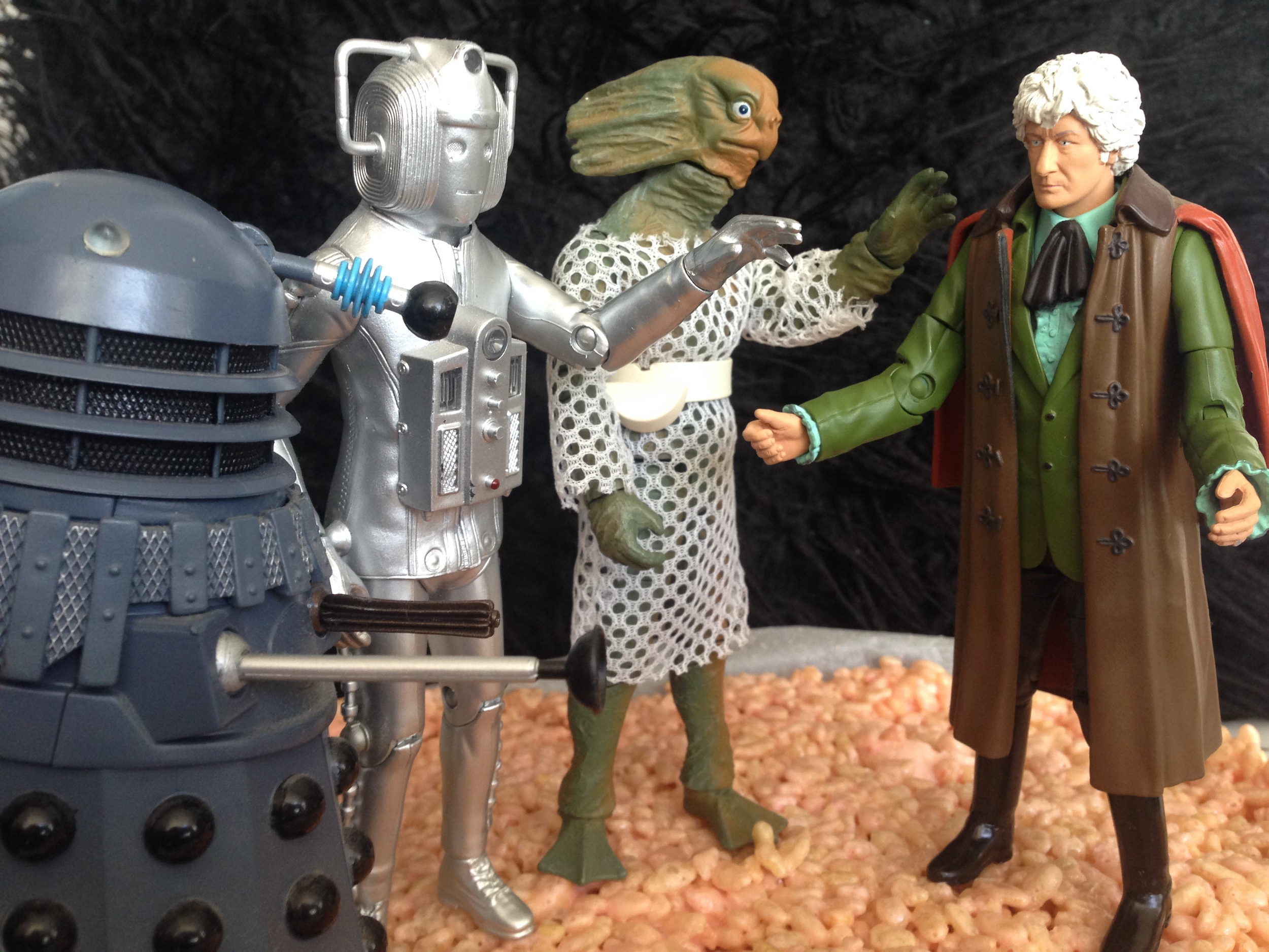 A tray of a slice made of rice bubbles with some Third-Doctor era character figures on top